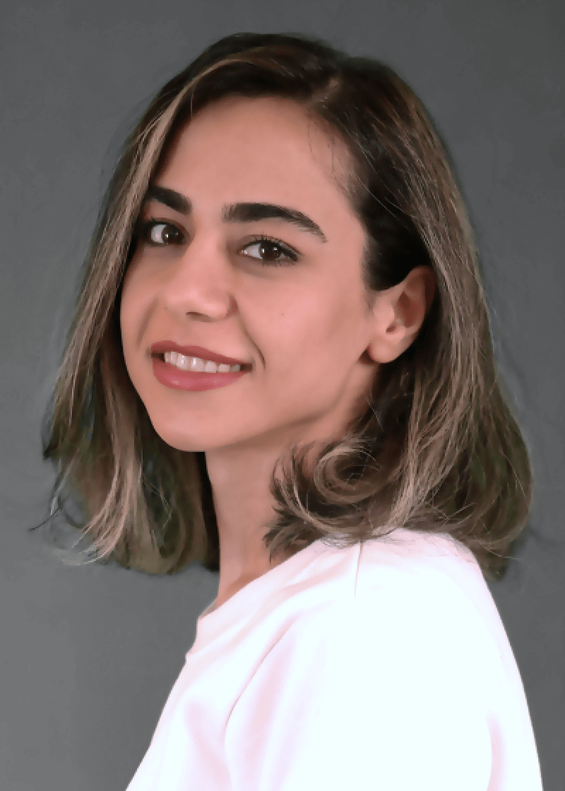 El Afroozan A woman with shoulder-length brown hair, smiling slightly, wearing a light pink top against a gray background.