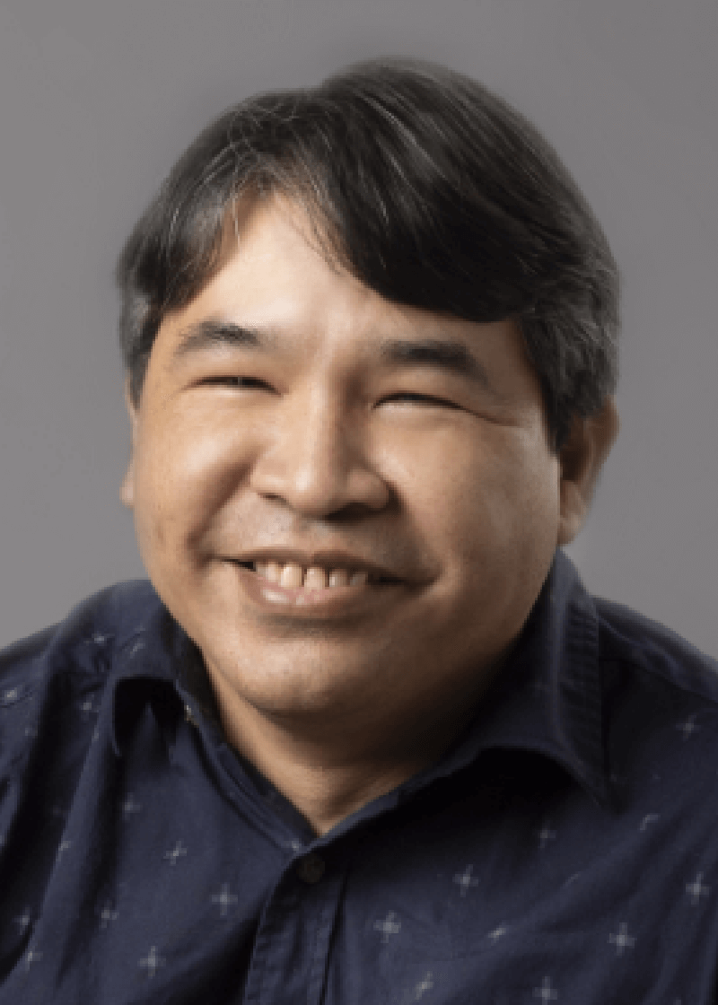 Jaime Wong A smiling man with dark hair and a dark patterned shirt against a gray background.