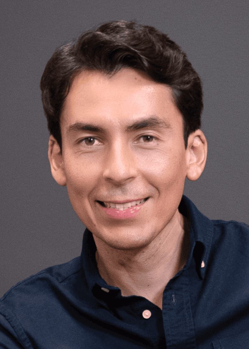 Rafael Hernandez A man with dark brown hair, wearing a dark blue shirt, smiling against a gray background.