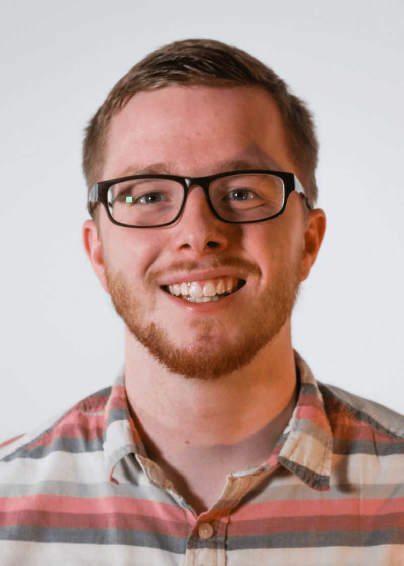 Scott Cooper A smiling man with glasses, a beard, and short hair wears a plaid shirt against a plain background.