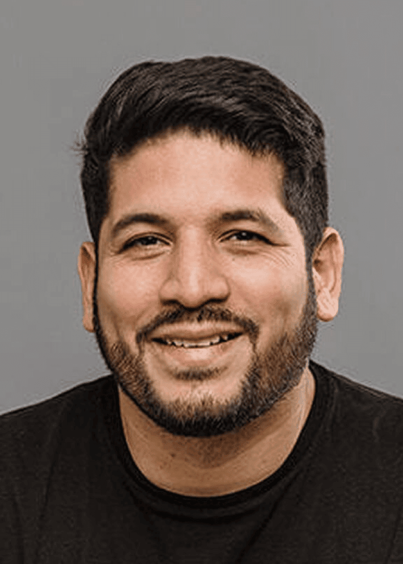 Giancarlo Rossi A smiling man with dark hair, a beard, and wearing a black shirt against a gray background.